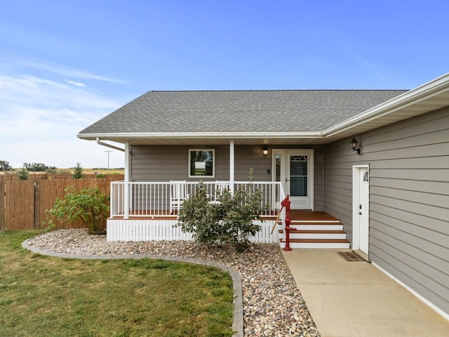 entrance to property with covered porch, a yard, fence, and roof with shingles