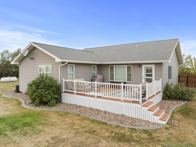 view of front of home with a shingled roof, a front yard, and a wooden deck