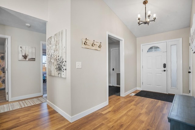 foyer featuring a notable chandelier, baseboards, vaulted ceiling, and wood finished floors