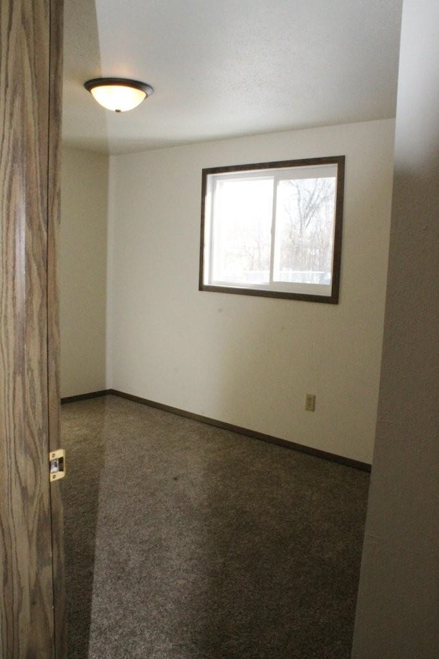 spare room featuring baseboards and dark carpet