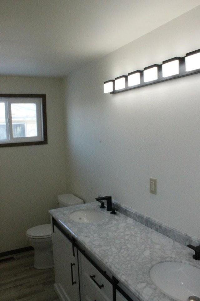 bathroom with double vanity, wood finished floors, a sink, and toilet