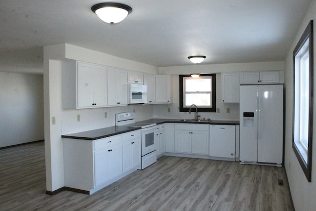 kitchen featuring dark countertops, light wood-style floors, white cabinets, a sink, and white appliances