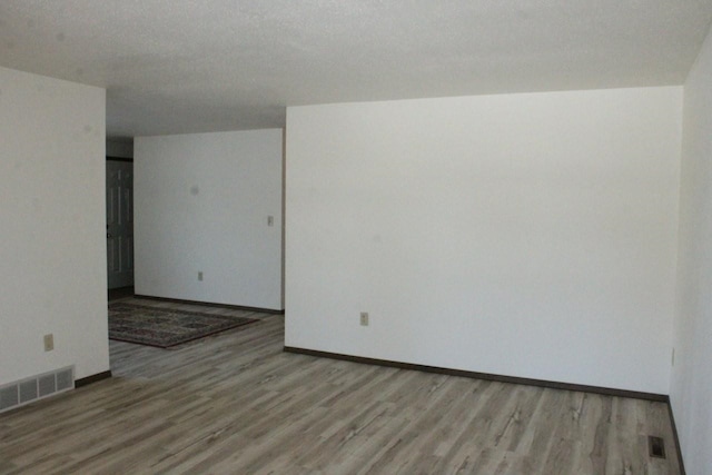 spare room featuring light wood-type flooring, visible vents, and baseboards