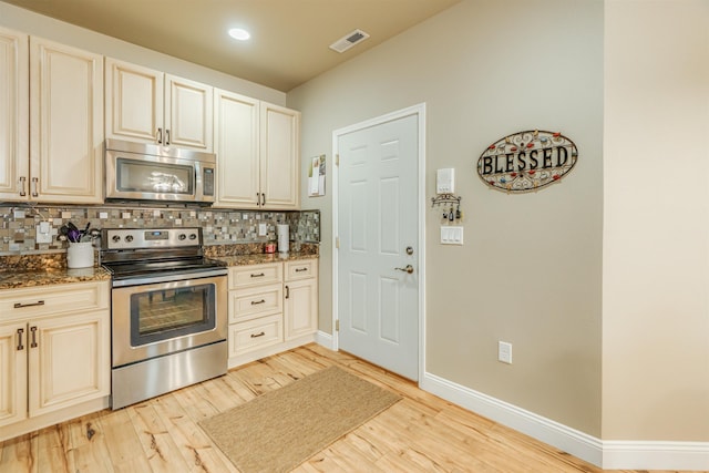 kitchen featuring stainless steel appliances, tasteful backsplash, visible vents, light wood-style floors, and dark stone countertops