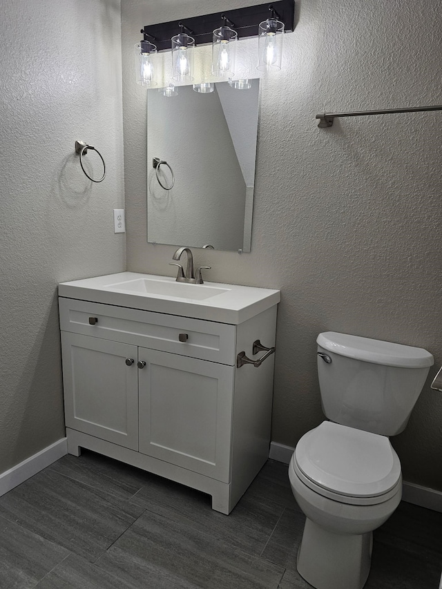 half bath with toilet, a textured wall, baseboards, and vanity