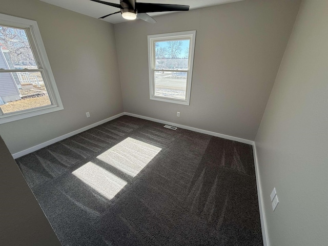 spare room featuring dark colored carpet, visible vents, ceiling fan, and baseboards