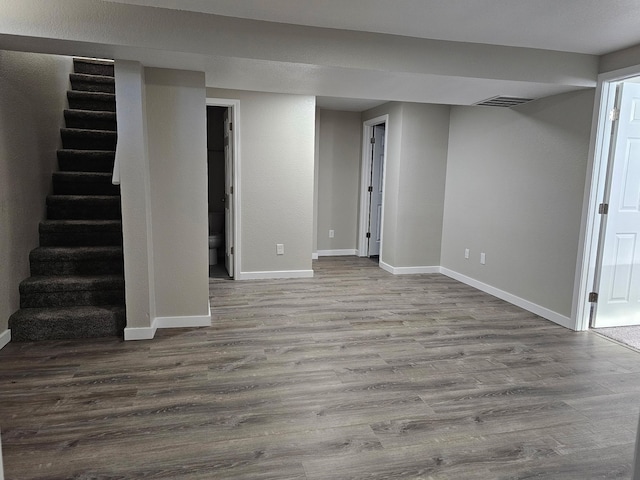 finished below grade area with dark wood-style floors, stairway, and baseboards