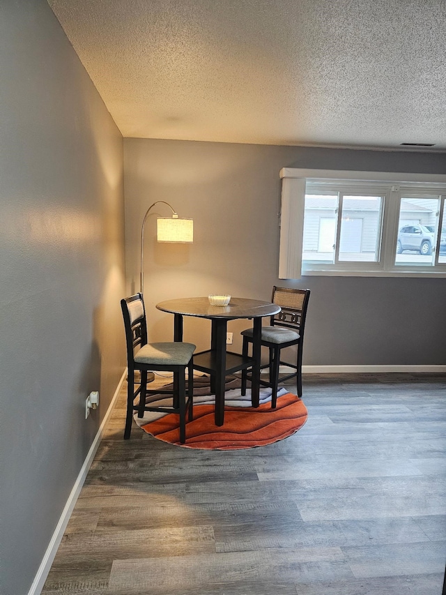 dining area featuring a textured ceiling, baseboards, and wood finished floors