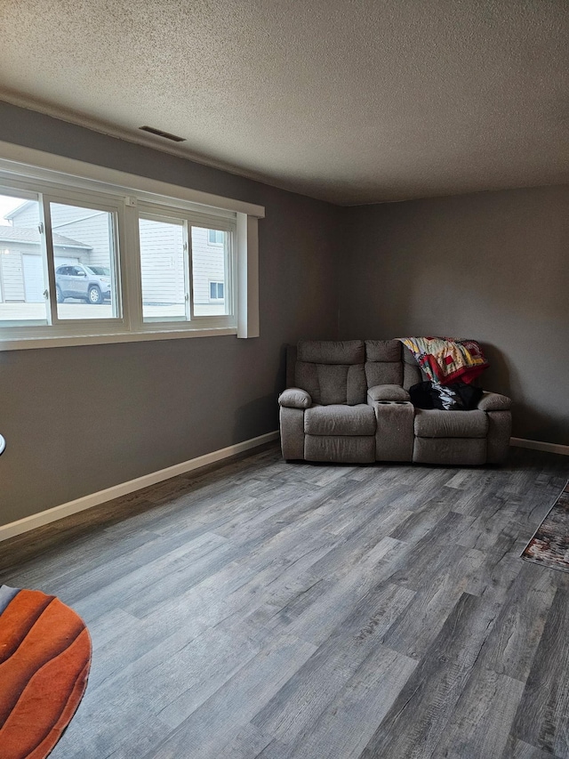 living area with a textured ceiling, wood finished floors, visible vents, and baseboards