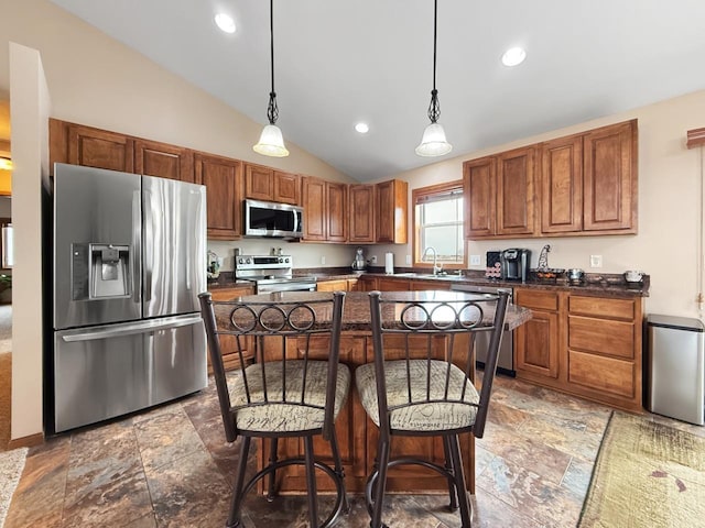 kitchen featuring dark countertops, appliances with stainless steel finishes, a kitchen breakfast bar, and a sink