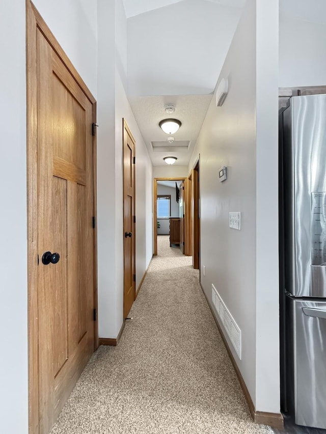 hall featuring baseboards, visible vents, and light colored carpet