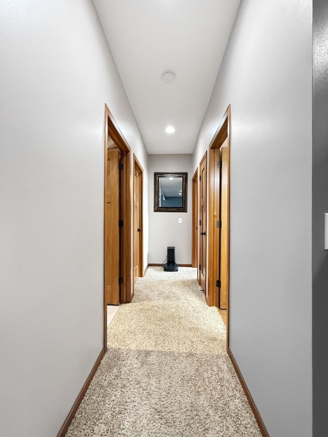 hallway with baseboards and light colored carpet