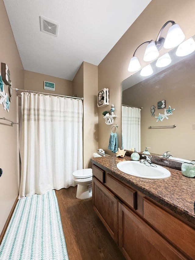 bathroom with toilet, vanity, wood finished floors, and visible vents