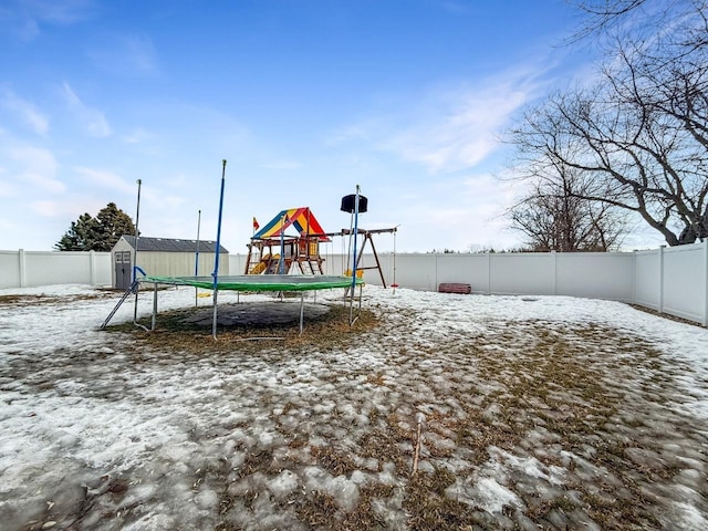 snow covered playground with an outbuilding, a playground, a fenced backyard, a shed, and a trampoline