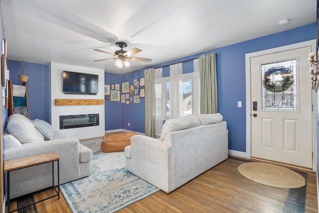 living room with ceiling fan, wood finished floors, a glass covered fireplace, and baseboards