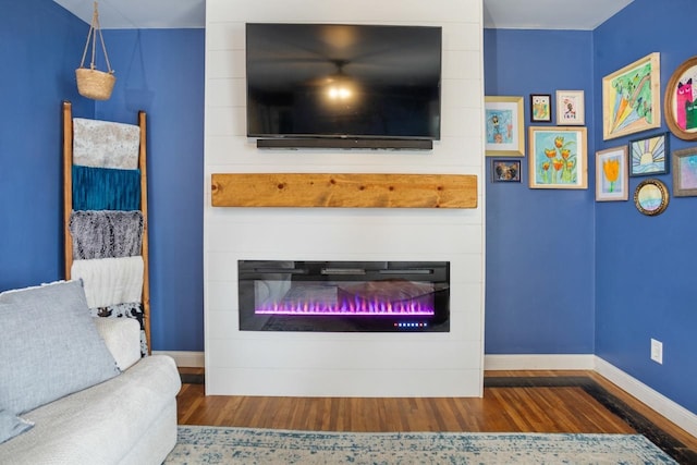 living room with a large fireplace, baseboards, and wood finished floors