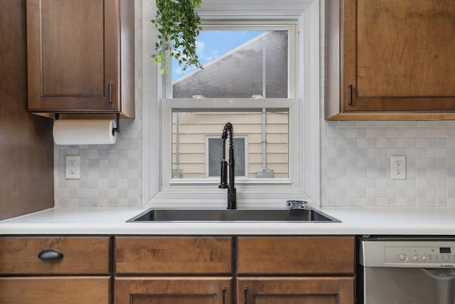 kitchen featuring light countertops, stainless steel dishwasher, backsplash, and a sink