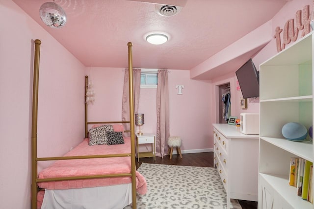 bedroom with visible vents, a textured ceiling, baseboards, and wood finished floors