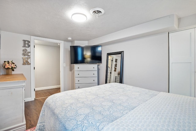 bedroom featuring a textured ceiling, visible vents, baseboards, a closet, and dark wood finished floors