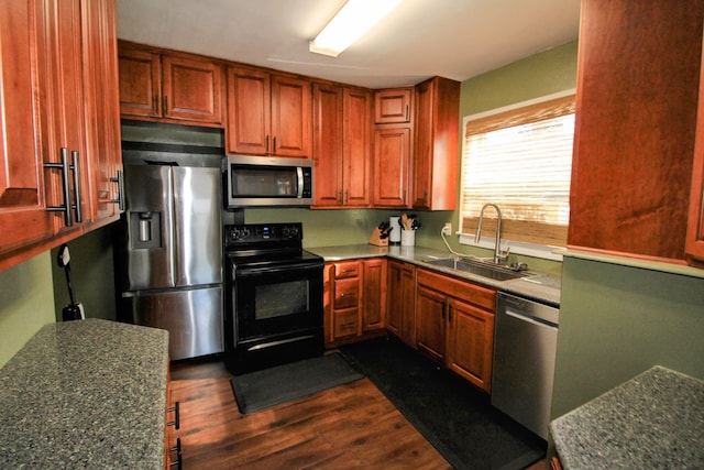 kitchen with dark wood-type flooring, a sink, appliances with stainless steel finishes, brown cabinetry, and dark countertops