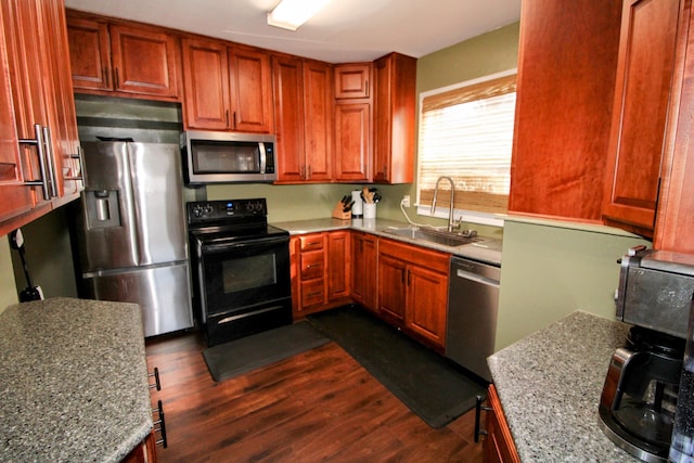 kitchen with stainless steel appliances, dark wood finished floors, a sink, and light stone counters