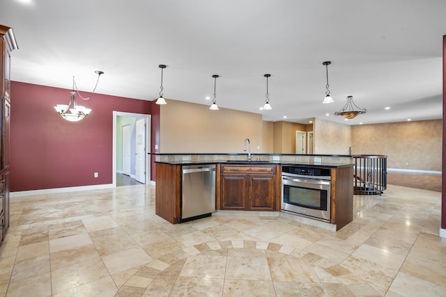 kitchen featuring baseboards, an island with sink, hanging light fixtures, stainless steel appliances, and a sink