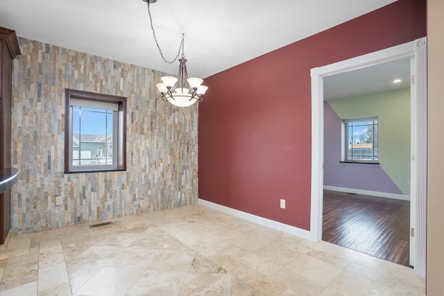unfurnished room featuring a notable chandelier, an accent wall, visible vents, and baseboards
