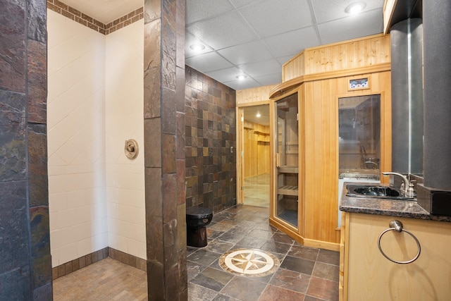 full bathroom featuring a drop ceiling, vanity, and stone tile floors