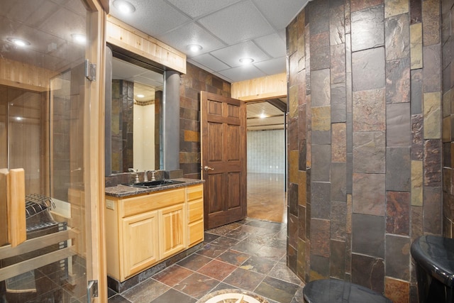 bathroom with a drop ceiling, vanity, and stone tile floors