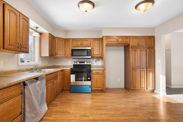 kitchen featuring stainless steel appliances, a sink, light countertops, light wood-type flooring, and brown cabinets