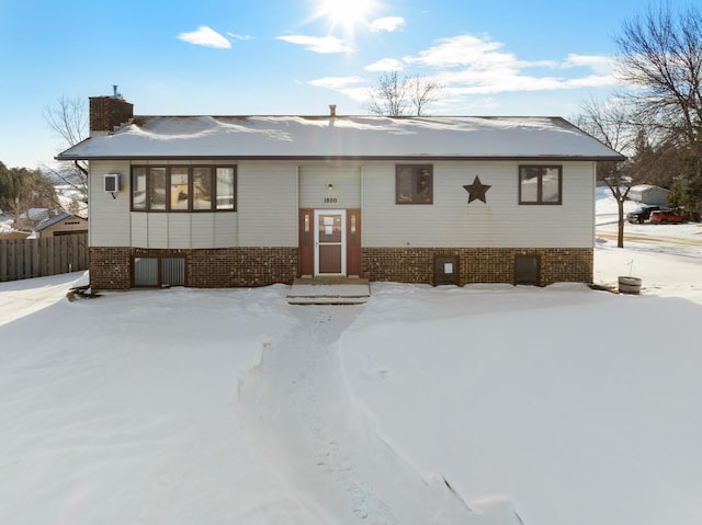 bi-level home with a chimney, fence, and brick siding