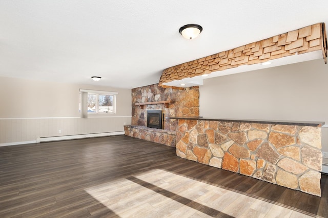 unfurnished living room featuring wainscoting, a baseboard radiator, wood finished floors, and a stone fireplace