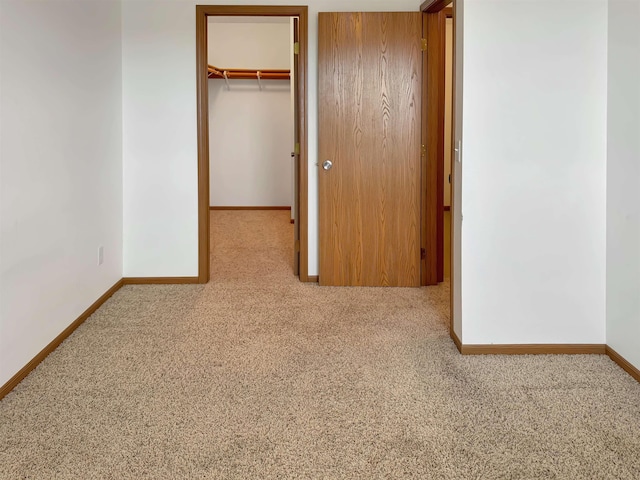 unfurnished bedroom featuring a walk in closet, a closet, baseboards, and carpet floors