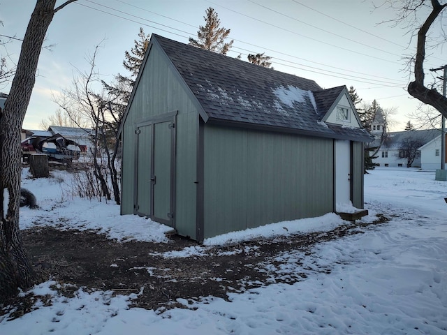 snow covered structure featuring an outbuilding and a storage unit