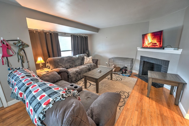 living area featuring a fireplace with flush hearth, baseboards, and wood finished floors