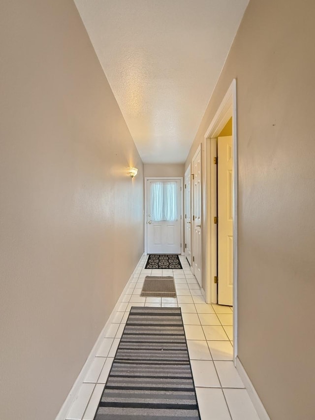 corridor featuring light tile patterned floors, baseboards, and a textured ceiling