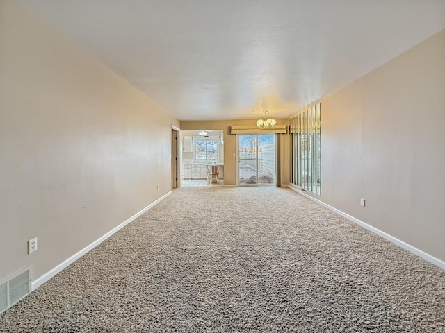 carpeted spare room featuring a notable chandelier, visible vents, and baseboards