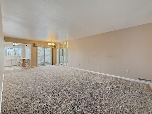 carpeted empty room with a textured ceiling, baseboards, visible vents, and a chandelier