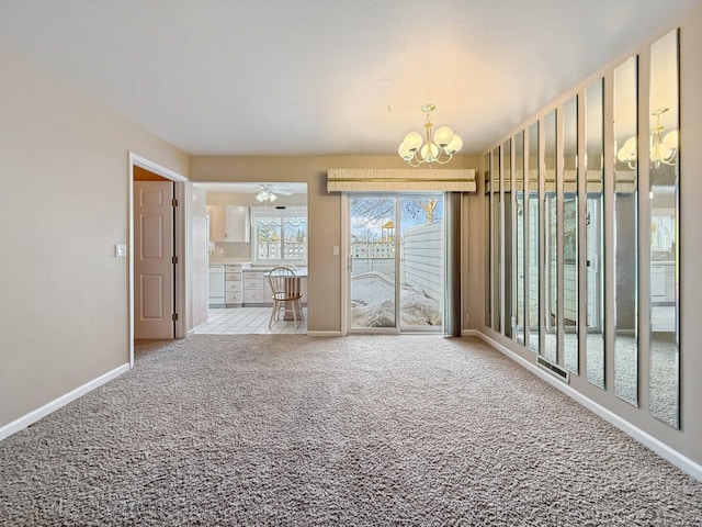 carpeted empty room featuring ceiling fan with notable chandelier and baseboards