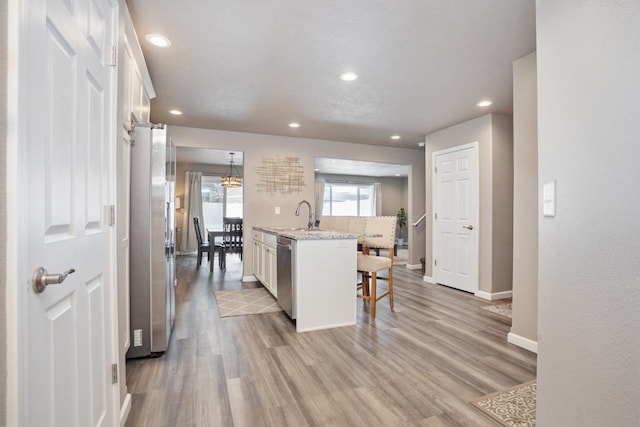 kitchen featuring white cabinetry, light wood-style flooring, a sink, appliances with stainless steel finishes, and a kitchen bar