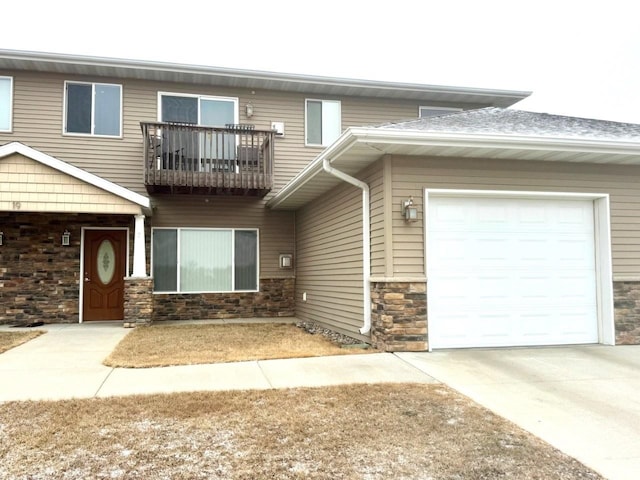 view of property featuring a garage, driveway, a balcony, and stone siding