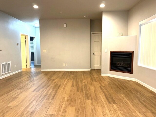 unfurnished living room featuring visible vents, baseboards, light wood-style floors, and a glass covered fireplace