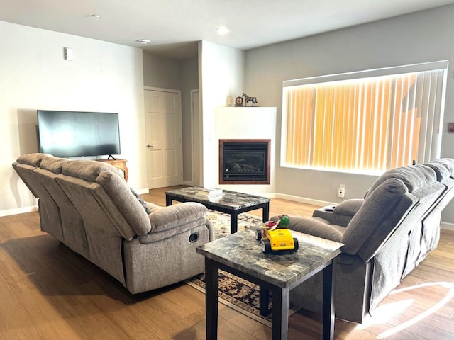 living room featuring a glass covered fireplace, recessed lighting, baseboards, and wood finished floors