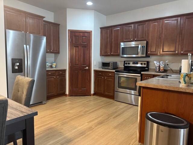 kitchen featuring a sink, recessed lighting, light wood-style floors, appliances with stainless steel finishes, and dark brown cabinets