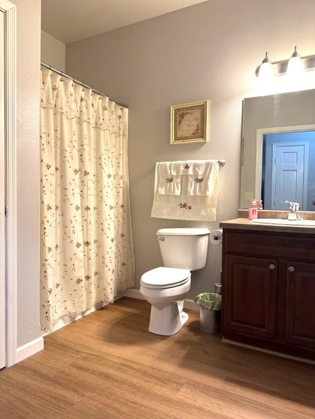 bathroom featuring baseboards, toilet, a shower with shower curtain, wood finished floors, and vanity