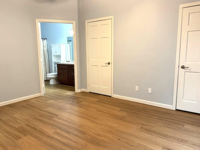 unfurnished bedroom featuring ensuite bathroom, baseboards, and wood finished floors