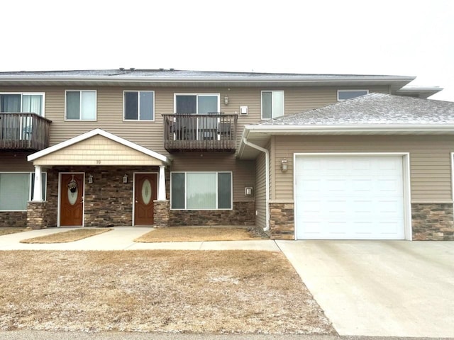 townhome / multi-family property featuring a garage, driveway, a balcony, and stone siding