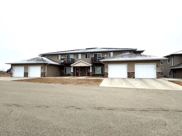 view of front of house with stone siding, a balcony, driveway, and a garage