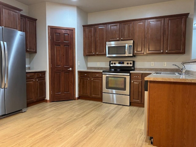 kitchen with a sink, stainless steel appliances, light countertops, and light wood finished floors