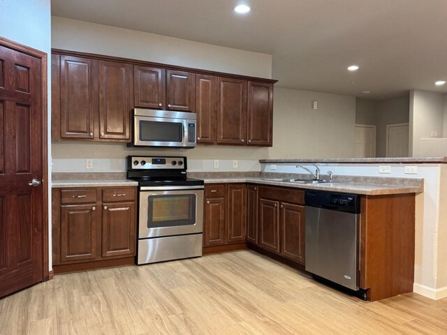 kitchen with recessed lighting, light wood-style flooring, a peninsula, stainless steel appliances, and a sink